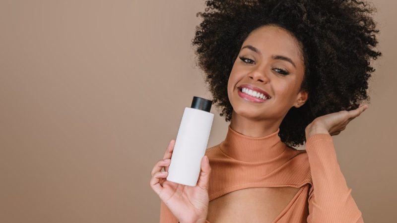 Beauty Latin woman with afro hairstyle. Brazilian woman. Holding blank shampoo packaging. Curly hair. Hair style. Pastel background.