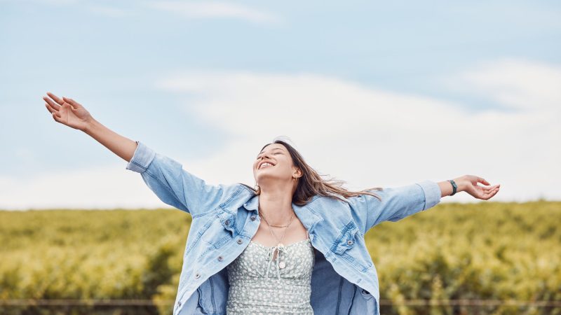 Happy, freedom and smile with woman in nature for peace, relax and youth with blue sky mockup. Journey, adventure and happiness with girl enjoying outdoors for summer break, vacation and holiday