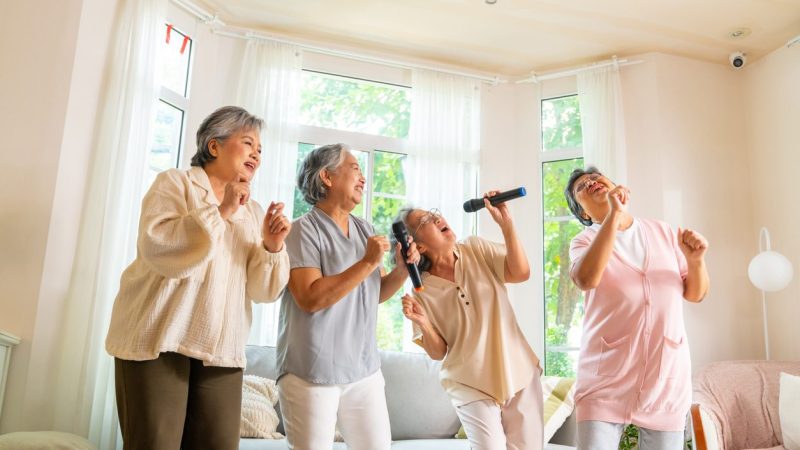 Group of Happy Asian senior women friends singing karaoke with dancing together in living room. Elderly retired people enjoy and fun indoor lifestyle spending time together with home entertainment.