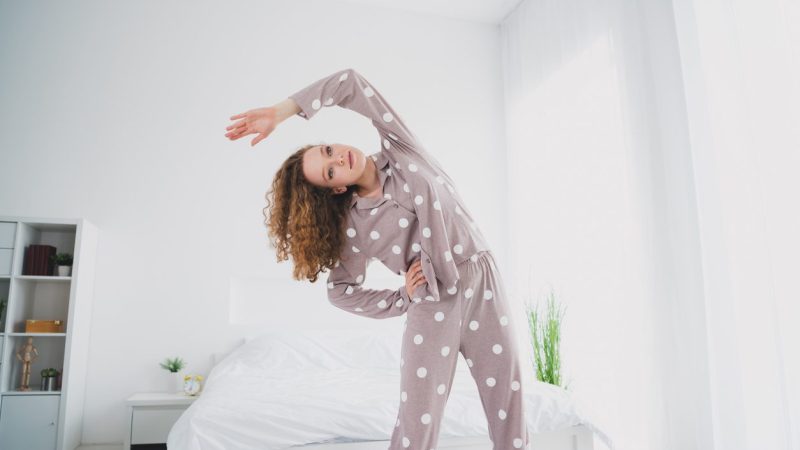 Photo of pretty young girl morning workout wear pajama bright bedroom apartment indoors.
