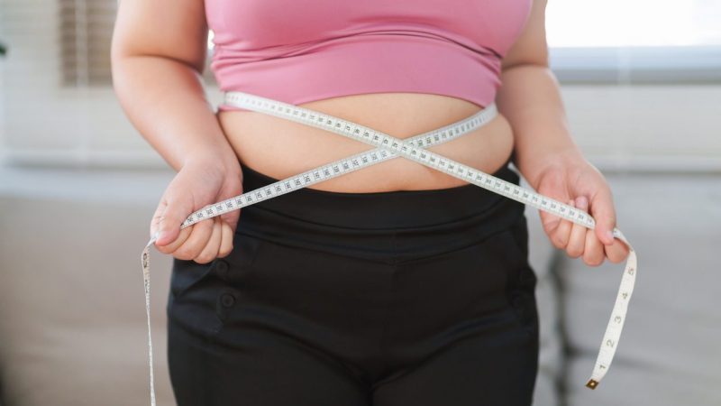 Close up overweight woman measuring her hip with tape measure.