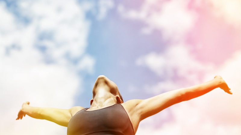 Happy young woman raised her arms and relaxing in nature. Woman wearing a black bra. She is listening the nature and tanning under the sun. Photo's toned with some color addition. Photo's taken from a little bit bottom.