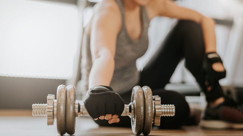 Happy smiling woman picking up dumbbell on gym floor for start fitness training