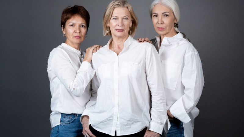 Portrait of beautiful mature women in white shirts posing at camera against the grey background